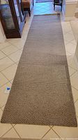 Full view of the taupe and grey carpet runner laid out on a tiled floor, showing its length and bound edges.