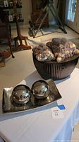 Silver tray with two large silver balls and brown metal container with bags of dried natural decorative items.