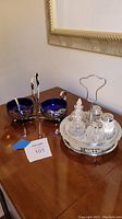 Overview photo showing both the silver cream and sugar set with blue glass inserts and the silver condiment carousel with 5 glass containers on a wooden surface.