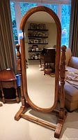 Front view of a full length medium oak framed mirror with oval shape and colonial style features, standing upright in a living room.