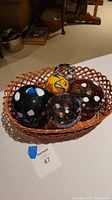 Four multicolored glass friendship balls in varying sizes and patterns arranged inside a wicker basket with a lattice design.