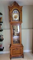 Full front view of grandfather clock showing wooden case, bonnet top, winding door and trunk with glass panel