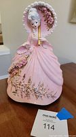 Front view of the Josef Originals pink lady figurine on a wooden surface next to a lot number tag.