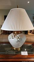 Full view of ceramic table lamp showing white pleated shade, ceramic base with floral detail, and brass accents