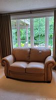 Front view of tan leather sofa positioned in front of window showing overall shape and condition