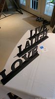 Three black painted decorative words: Live, Laugh, and Love arranged in a row on white table surface.
