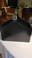 Front angle showing the black faux alligator skin textured magazine holder with curved handle strap and silver buckle.