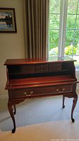 Full view of mahogany writing desk with Queen Anne legs in front of a window.