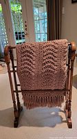 Front view of oak blanket stand with taupe crocheted afghan draped over it.