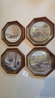 Full shot of all four framed plates laid on carpet floor, each frame is octagonal with a brown wood finish, plates round with rural scenes.