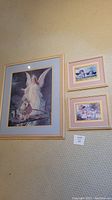 Three framed angel pictures hung on a beige textured wall, one large and two smaller hung side by side