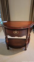 Full view of mahogany half-moon table showing polished top, turned legs, drawer with brass pull and lower shelf