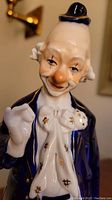 Close-up of the first porcelain clown figurine, showing detailed facial expression, blue jacket, white bow tie with gold highlights, and black hat.