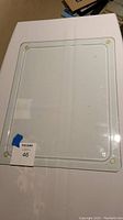 Clear glass hot plate or cutting board, rectangular with rounded corners and four corner pads, laying flat on table