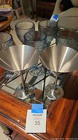 Five light blue tinted ribbed glasses and two stainless steel martini glasses on mirrored surface