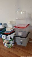 Stack of various empty plastic storage bins and containers including clear bins with red lids and a decorative dog image bin.
