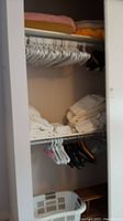 Photo showing folded white sheets, blankets, pillowcases on closet shelves along with white and black hangers on hanging rod.