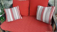 Front view of outdoor patio glider showing red seat cushion and two striped toss pillows.