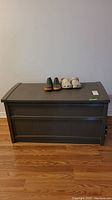 Photo of brown outdoor storage bin with two pairs of footwear on top against a wall