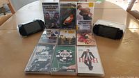 Two PSP consoles, nine UMD games, arranged on table for overview
