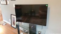 Samsung 42 inch LED TV with reflective screen positioned on a glass table with base missing, showing cables underneath.