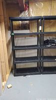 First shelving unit fully assembled with 5 black plastic ventilated shelves.