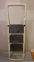 Full view of the foldable step ladder showing three steps and white frame.