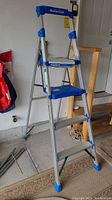 Mastercraft aluminum compact step ladder displayed upright indoors, showing overall structure and blue safety accents.