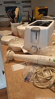 Lot overview showing Black & Decker toaster, Braun hand mixer, assortment of small CorningWare dishes, and some utensils on the kitchen counter.