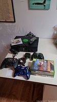 Original Xbox console with controllers, remote control, and game discs on table.