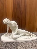 Side view of white sculpture showing seated male Gaul warrior with curly hair, leaning on arm, head bowed.