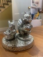 Front and slight left angle view showing two silver-colored squirrels on a textured round base.