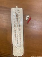 Full length view of handheld cribbage board showing scoring tracks and pegs beside the board.