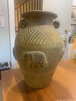 Front view of large pottery vase showing elephant-shaped carvings and geometric patterns.