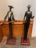 Photo of two slender metal statues of a man and a woman on wooden bases, showing full front view.