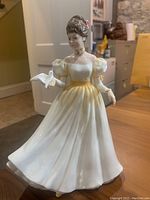 Front view of Kathleen Royal Doulton porcelain figurine showing lady in white and yellow dress holding a white dove.
