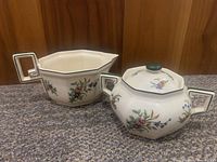 Photo showing both sugar bowl and creamer with floral pattern and green trim on carpeted floor with wooden background.
