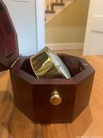 Close-up photo showing clock inside octagonal wooden box with brass knob on front and the clock angled.