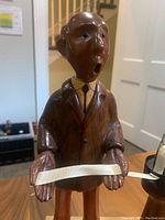 Front and upper body view of hand-crafted wooden stockbroker figurine holding ticker tape.
