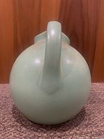 Back view of the teal ceramic pitcher showing single handle and rounded body shape.