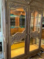 Front view of walnut china cabinet showing carved wood doors with glass panels and mirrored interior back.