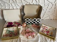Overview of Christmas decoration lot showing boxed ornaments including lipsticks, purses, ballerina ornaments, pink glass and pearl-like garland, and decorative pieces.