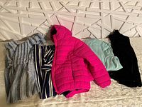 Photo showing all five clothing items laid out: pink puffer jacket, two rompers, mint green sweater, and soft black vest