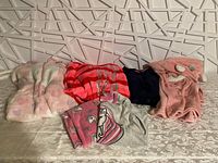 Assorted girls sleepwear laid out on a patterned surface, includes robes, pajamas, and nightgown pieces in various colors and prints.