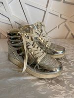 Right side angled view of pair of silver metallic Justice girls high-top running shoes with white laces, sitting on a patterned cloth surface.