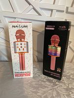 Photo showing packaging of two wireless karaoke microphones, one rose gold and one in black box with LED speaker indication.