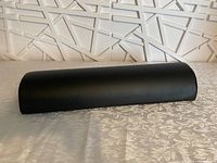 Black semi-cylindrical back support pillow placed on fabric surface with geometric wall background.