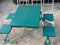 View of the green picnic table with four attached seats and foldable aluminum legs, showing the table fully open and assembled on a stone patio.