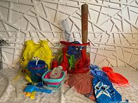 Overview of kids sand toys including buckets, molds, red plastic cup, and yellow life jacket arranged on surface