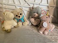 Photo of four new stuffed animals: white unicorn, beige teddy bear in blue hoodie, grey bear with heart, pink unicorn